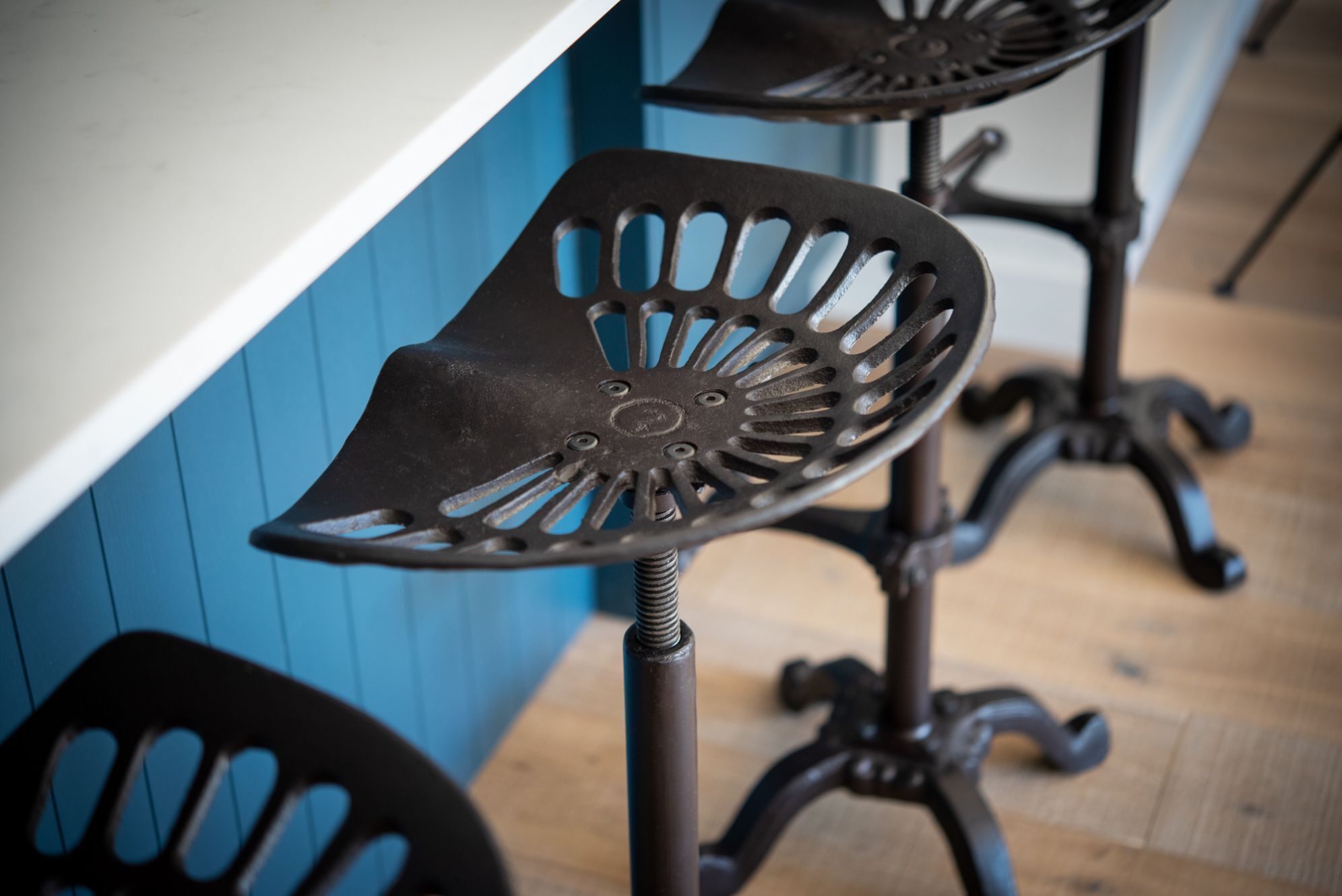 A close-up of a metal bar stool with a unique cut-out design, positioned against a blue wall.
