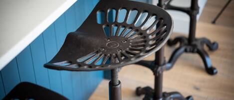 A close-up of a metal bar stool with a unique cut-out design, positioned against a blue wall.