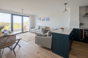 Relax in this serene living space with a sliding glass door leading to an outdoor area, a sofa, and a kitchen area with a small table and vase of flowers.