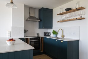 Una cocina moderna con armarios azul oscuro, encimera blanca, horno empotrado, tostadora y un lavabo con grifo dorado.