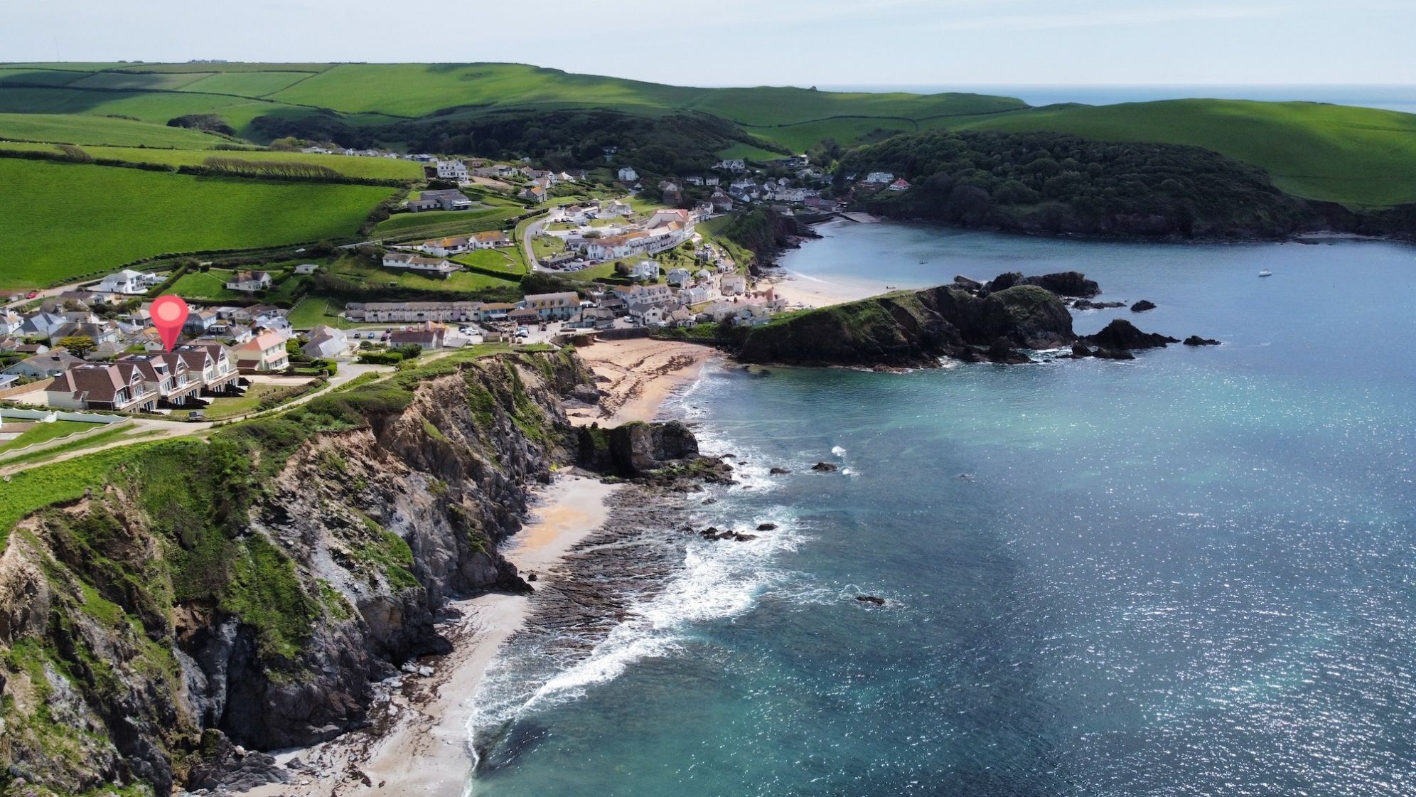 A coastal town with a beach, houses, and a cliff overlooking the sea.