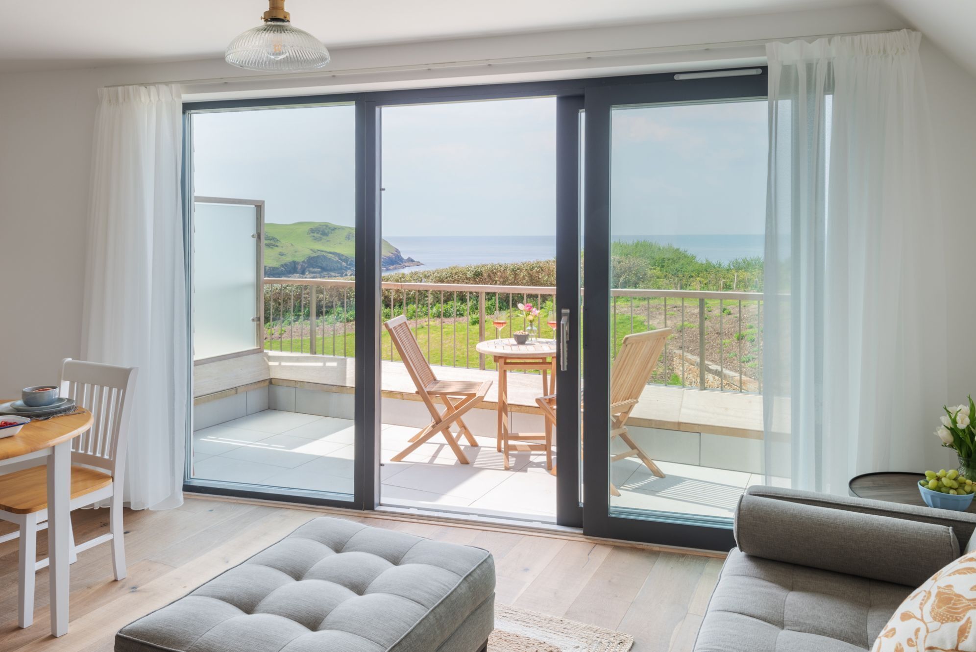 A modern living room with a sliding glass door leading to a balcony with a scenic ocean view.