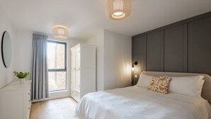 A bedroom with a large bed, a wardrobe, a mirror, and a window with curtains.
