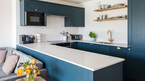A modern kitchen with blue cabinets, a white countertop, a built-in oven, and a coffee machine.