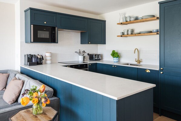 A modern kitchen with blue cabinets, a white countertop, a built-in oven, and a coffee machine.