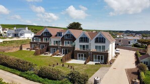 A large, modern house with multiple levels and balconies, surrounded by a well-maintained lawn and a stone wall.