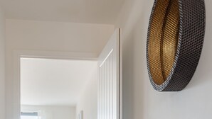 A hallway with a wooden console table, a white vase with flowers, and a textured wall hanging.