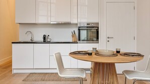 Eine moderne Küche mit weißen Schränken, einem eingebauten Ofen und einem runden Holztisch mit zwei Stühlen.