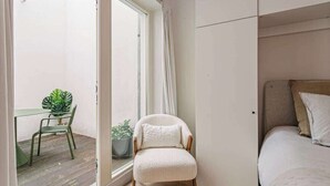 Ein kleiner, gemütlicher Raum mit einer Schiebetür aus Glas zum Balkon, einem Bett mit Kopfteil, einem Sessel und einem Tisch mit einem Topfblumen.