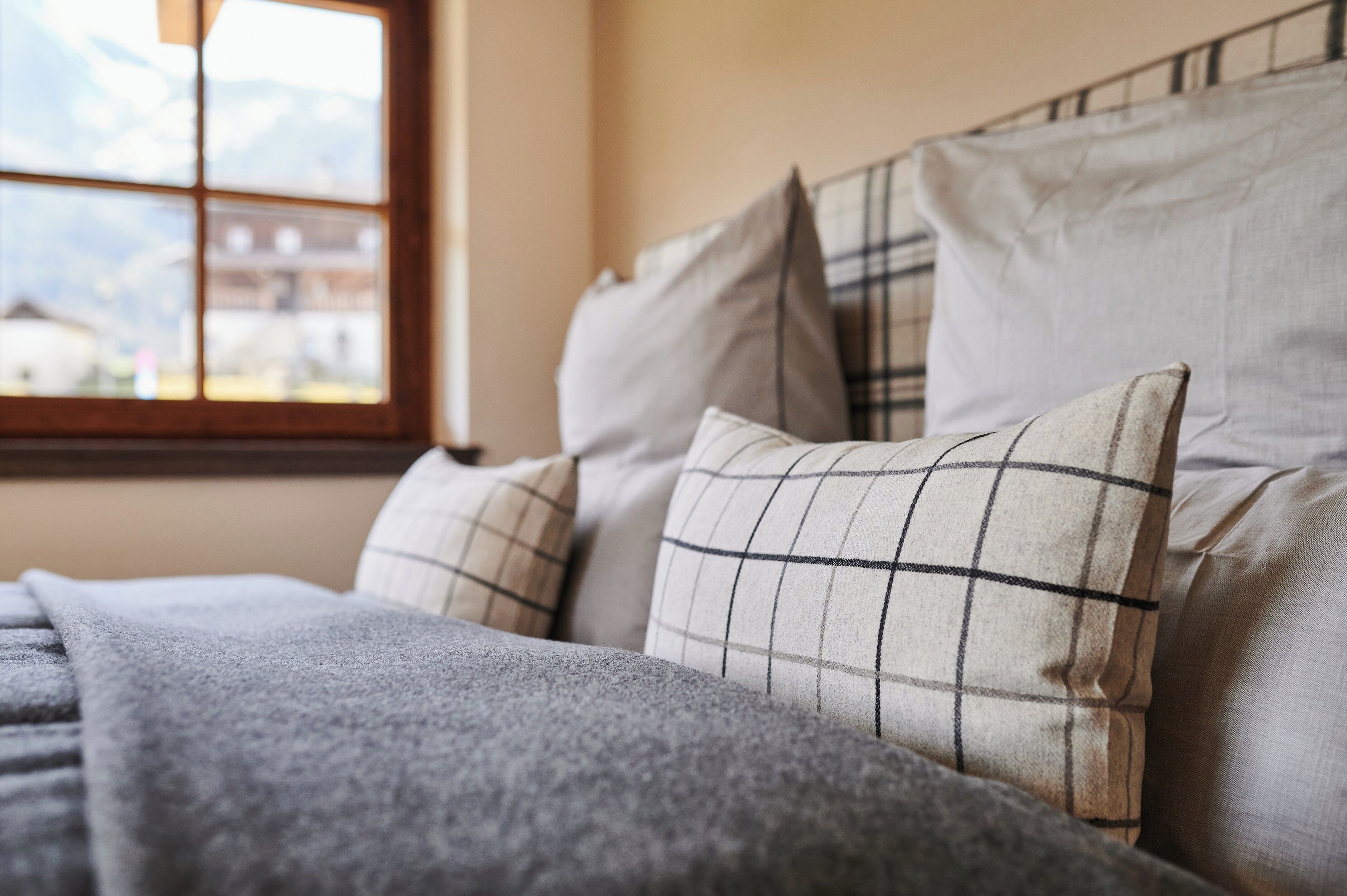 Un lit avec une couverture grise et des oreillers à motifs à carreaux.