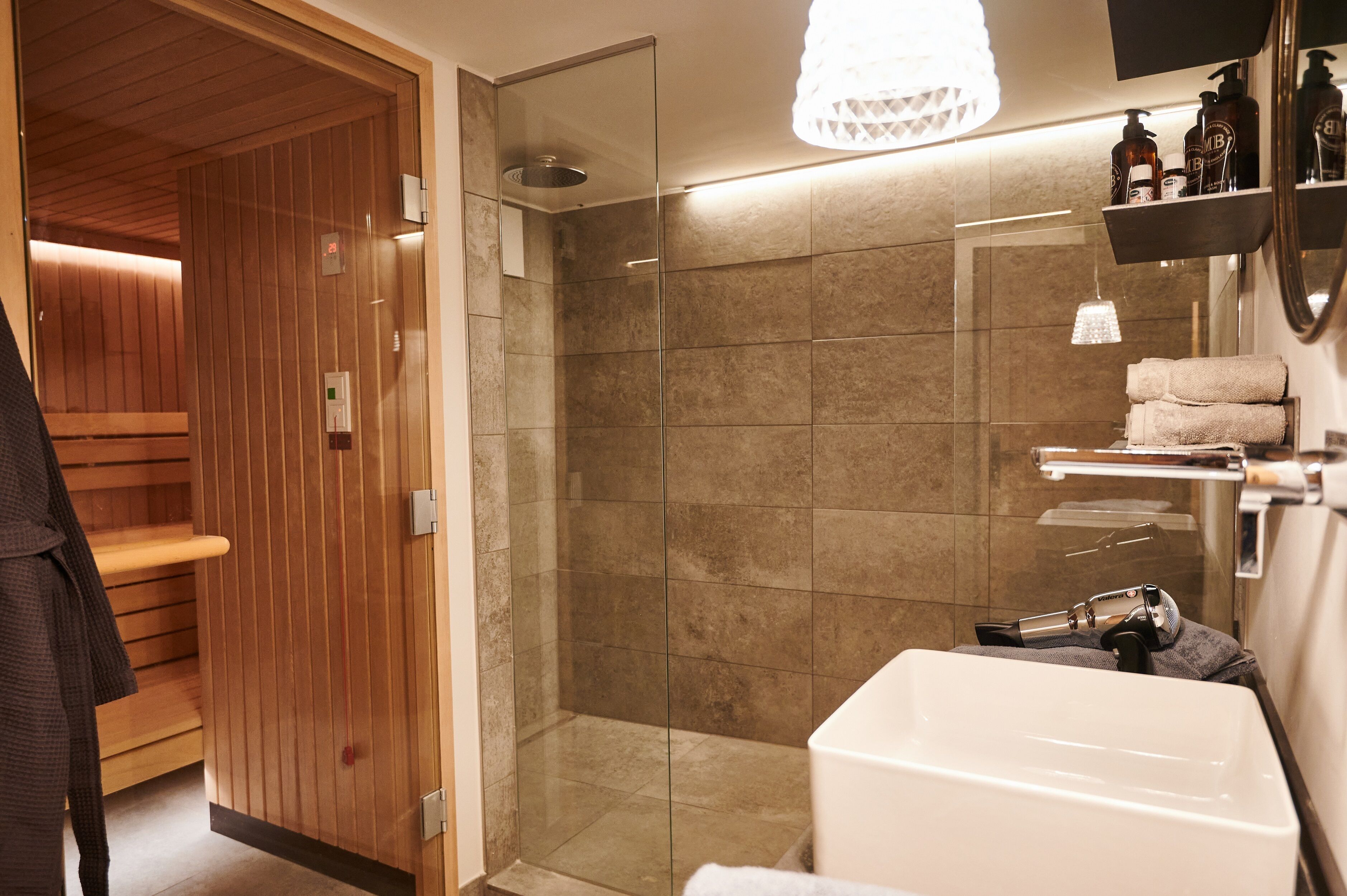 A modern bathroom with a glass-enclosed shower, a white bathtub, and wooden paneling in the adjacent room.