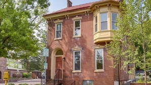 A two-story brick building with a red roof, a bay window on the second floor, and a front door with a small porch.