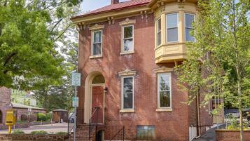 A two-story brick building with a red roof, a bay window on the second floor, and a front door with a small porch.