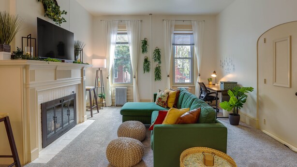 A living room with a fireplace, green sofa, ottomans, and a television.