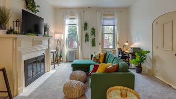 A living room with a fireplace, green sofa, ottomans, and a television.