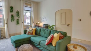 A green sectional sofa with multiple cushions, a wicker side table, and a small round ottoman.
