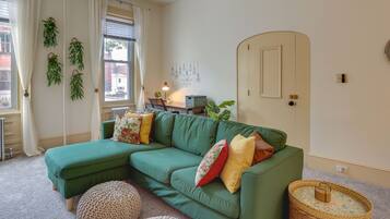 A green sectional sofa with multiple cushions, a wicker side table, and a small round ottoman.