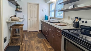 A compact kitchen with wooden flooring, a built-in microwave, a stove, and a window with blinds.