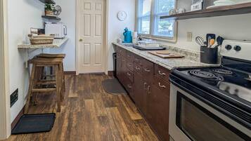 A compact kitchen with wooden flooring, a built-in microwave, a stove, and a window with blinds.