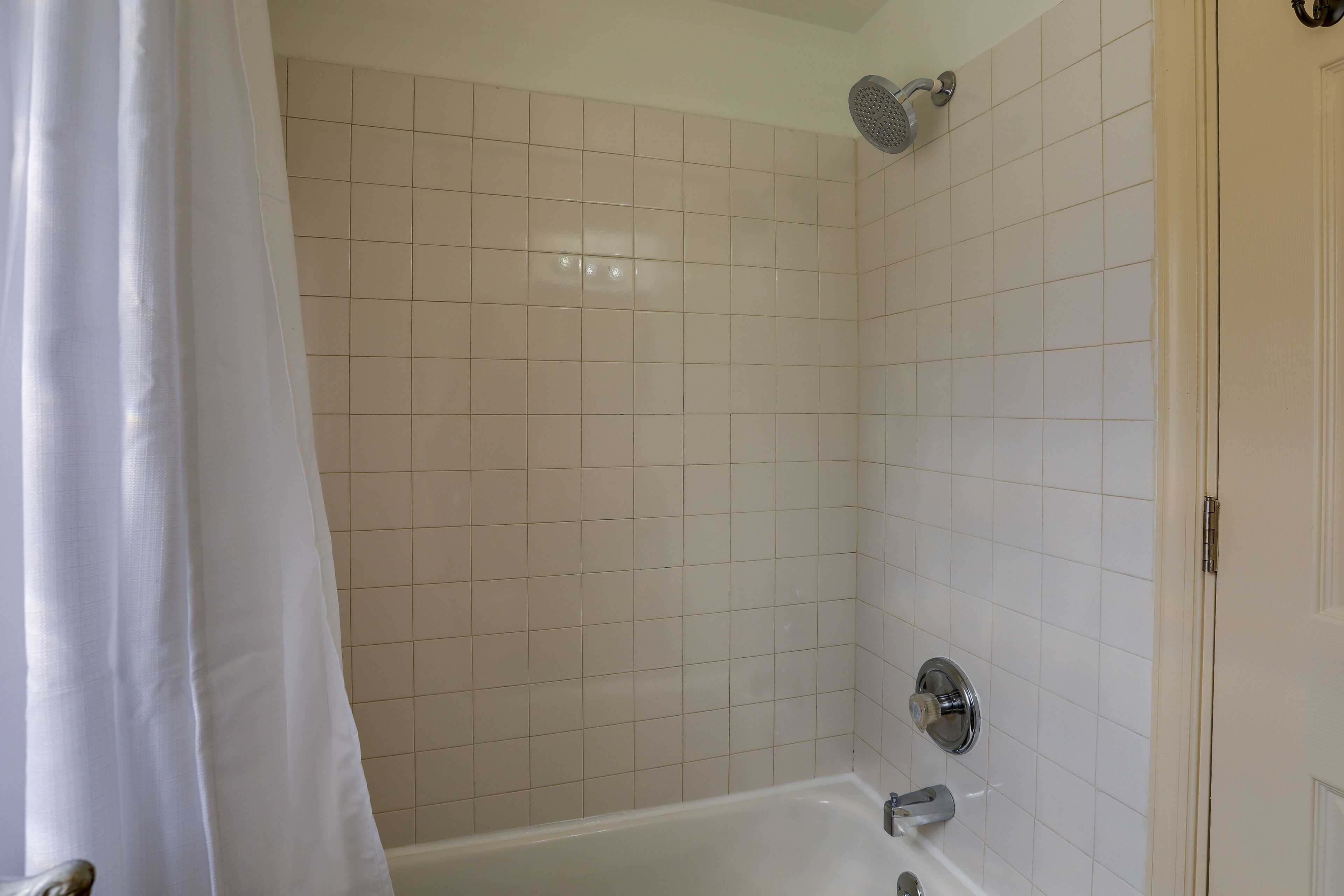 Een badkamer met witte betegelde wanden, een douche en een bad.