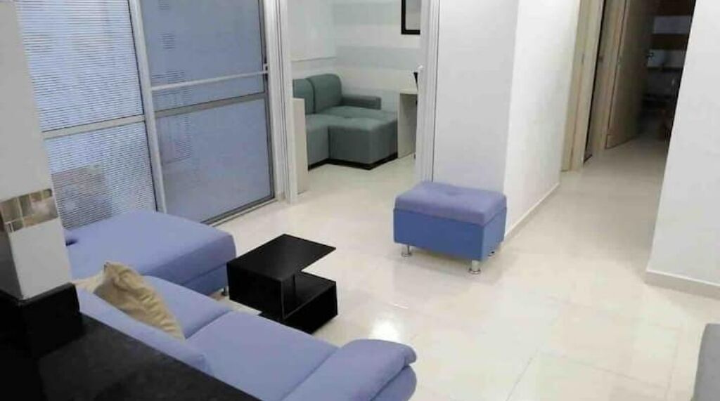 A modern living room with a blue sofa, a small black coffee table, and a grey ottoman.
