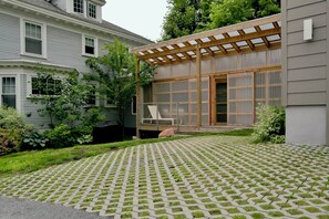 Un patio trasero residencial con un patio empedrado, una pérgola de madera y un área de estar cubierta.