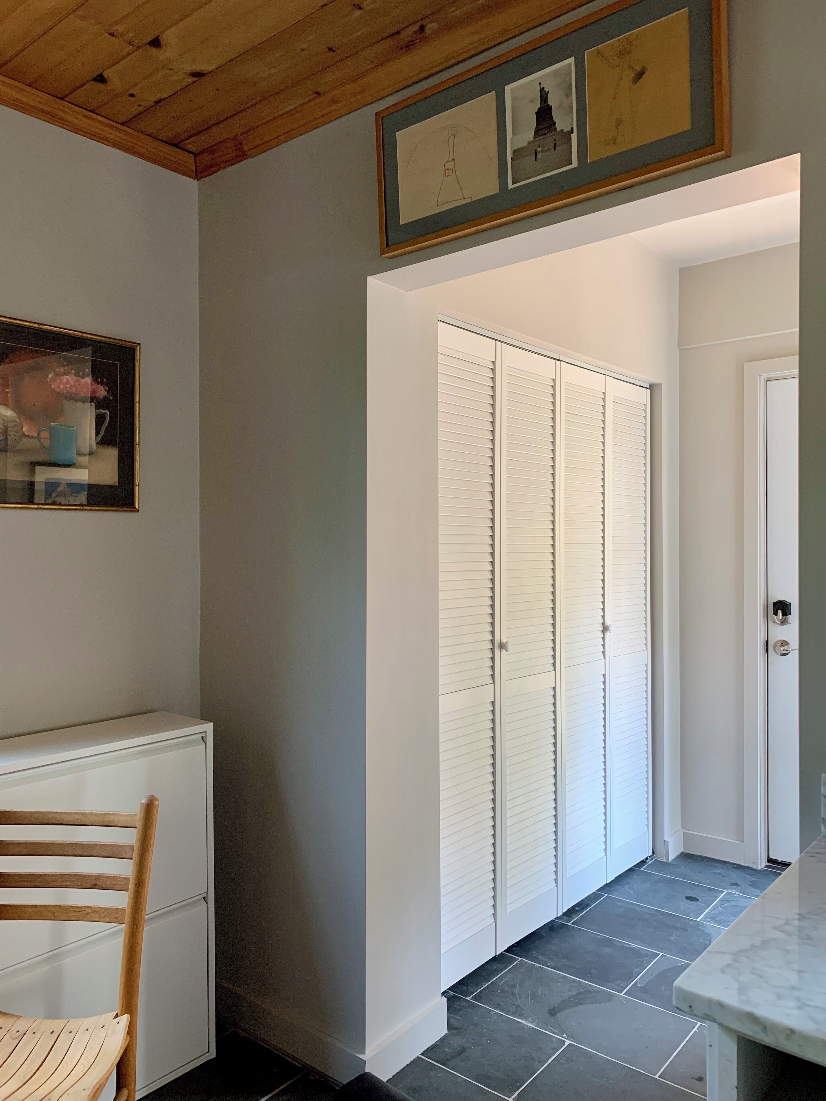 A hallway with a white door, a wooden chair, and a framed picture on the wall.
