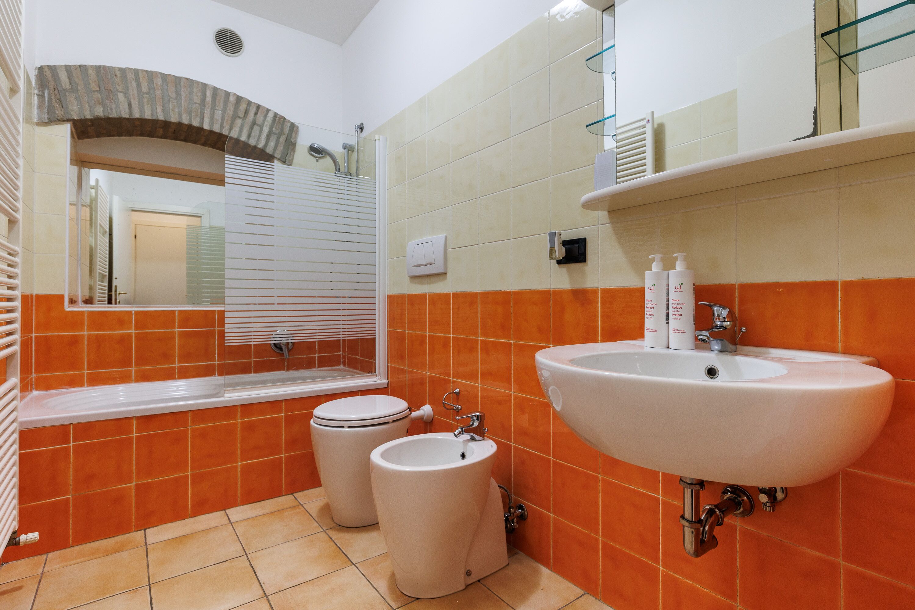 A bathroom with a white sink, two toilets, and orange tiles.