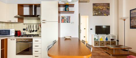 Eine moderne Küche mit weißen Schränken, einem Holzespeisetisch und einem Fernseher im Wohnbereich.