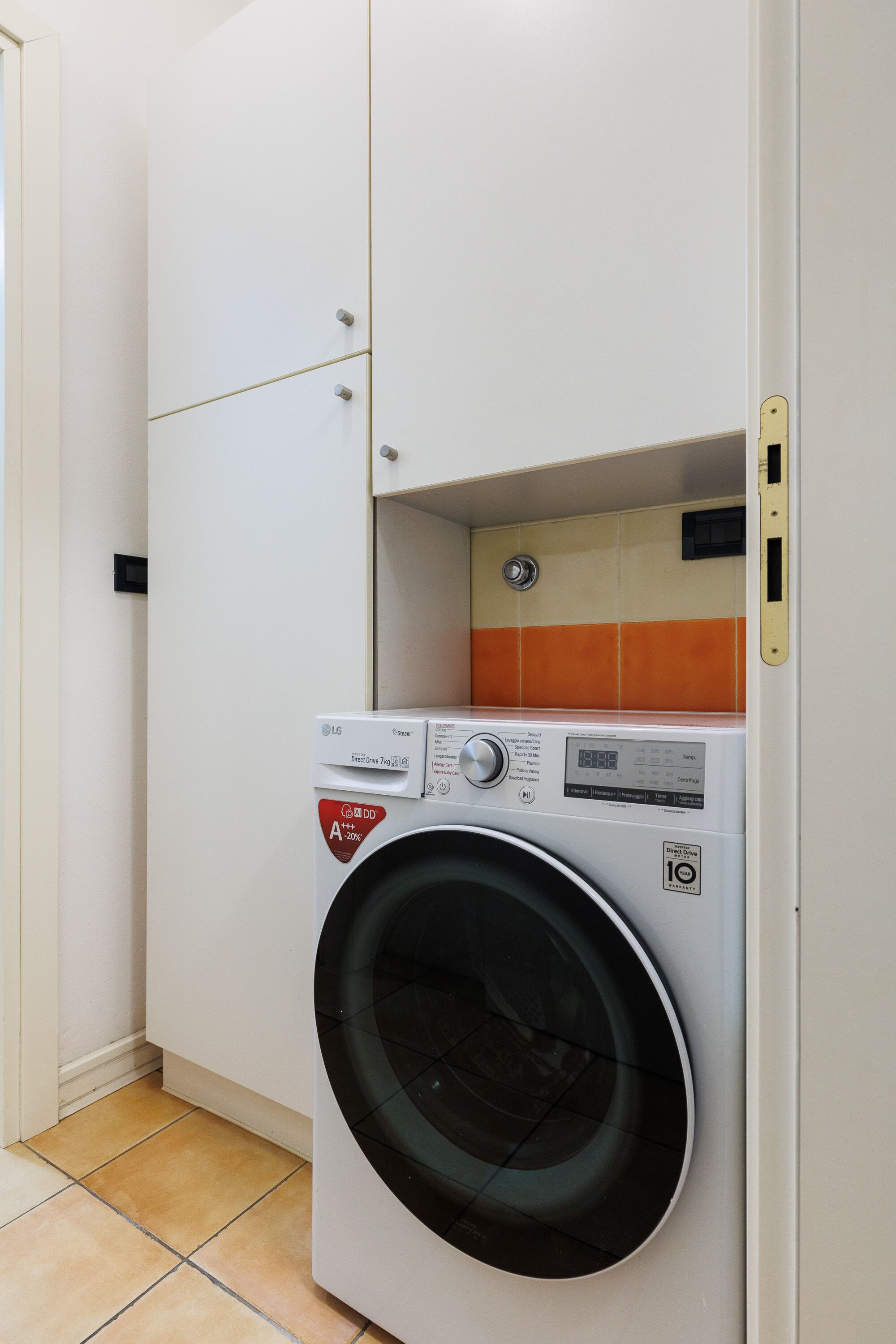 Ein kompakter Waschraum mit einer Waschmaschine mit Frontlader, einem Schrank darüber und einer gefliesten Rückwand.