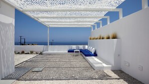A modern outdoor seating area with a white pergola, a blue sofa, and a small table. - Thadeos Villa (Santorini)