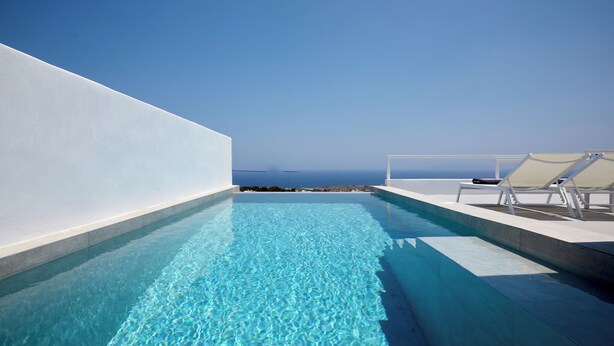 A rooftop infinity pool with clear blue water, white walls, and a view of the ocean. - Thadeos Villa (Santorini)