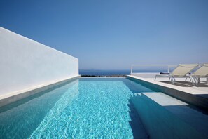 A rooftop infinity pool with clear blue water, white walls, and a view of the ocean. - Thadeos Villa (Santorini)