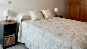 A bedroom with a large bed, two bedside tables with lamps, a wooden wardrobe, and two wall-mounted paintings. - Preciosa Vivienda Para Vacaciones a 50m de la Playa de Altar (Barreiros)