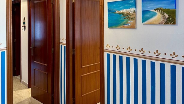 A hallway with wooden doors, a tiled floor, and two wall-mounted paintings of coastal scenes. - Preciosa Vivienda Para Vacaciones a 50m de la Playa de Altar (Barreiros)