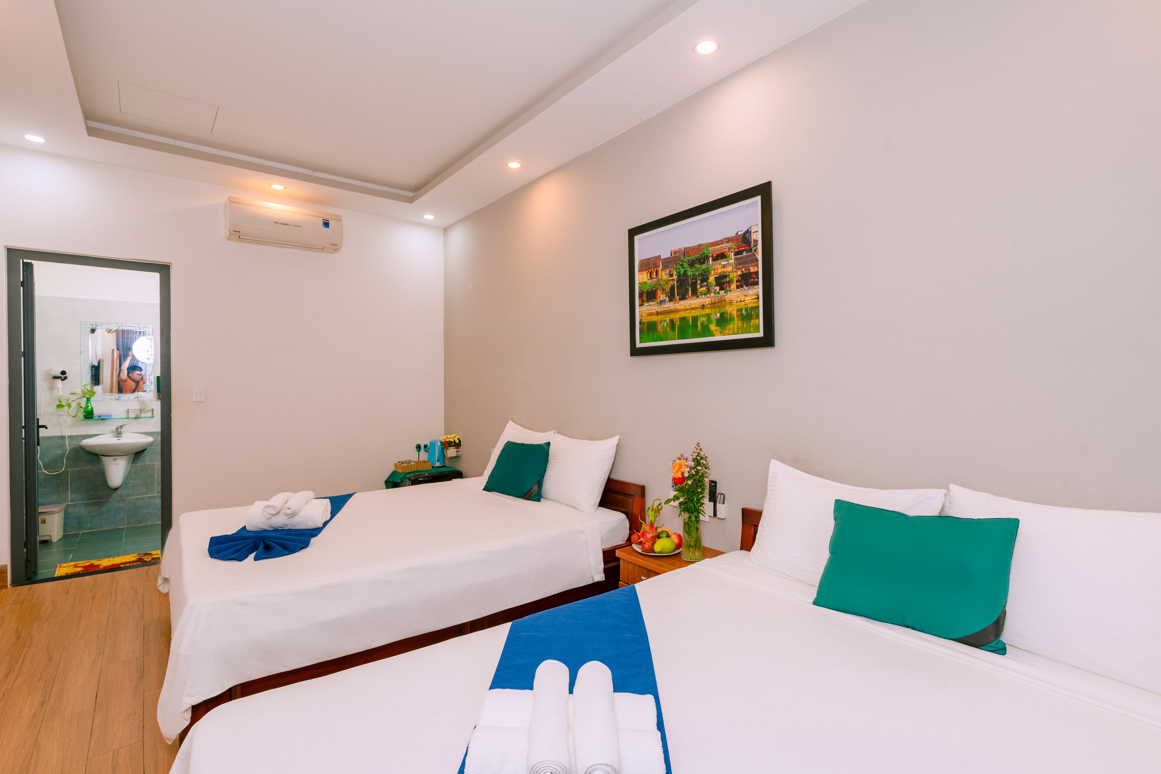 A hotel room with two beds, a bathroom, and a painting on the wall.