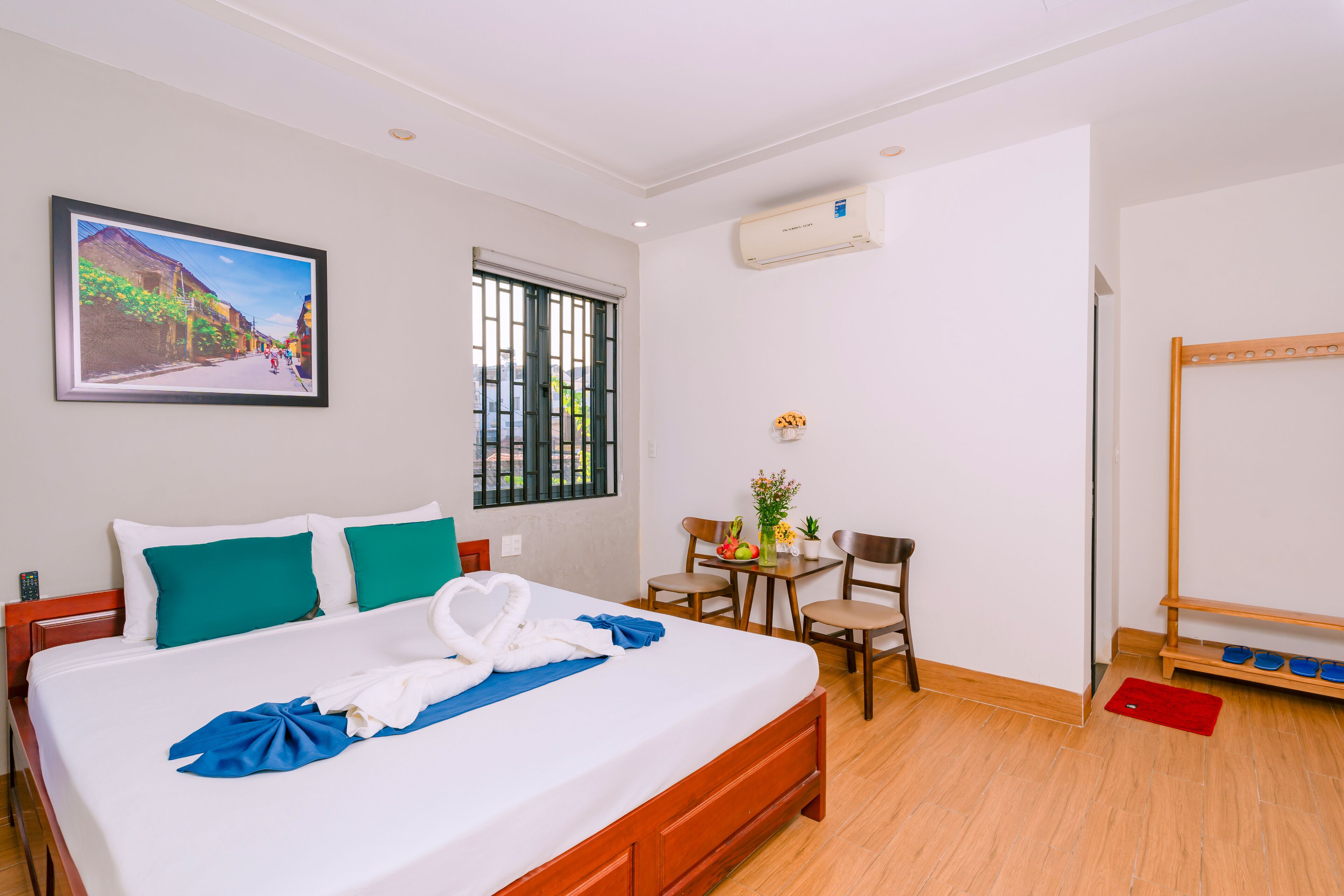 A hotel room with a bed, a desk, a chair, a small table with a vase, and a mirror.