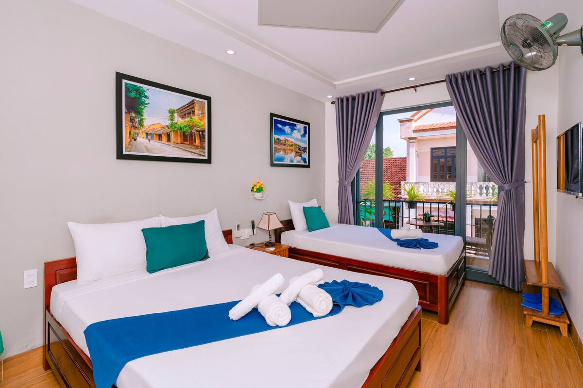 A hotel room with two beds, a balcony with a view, and a fan.