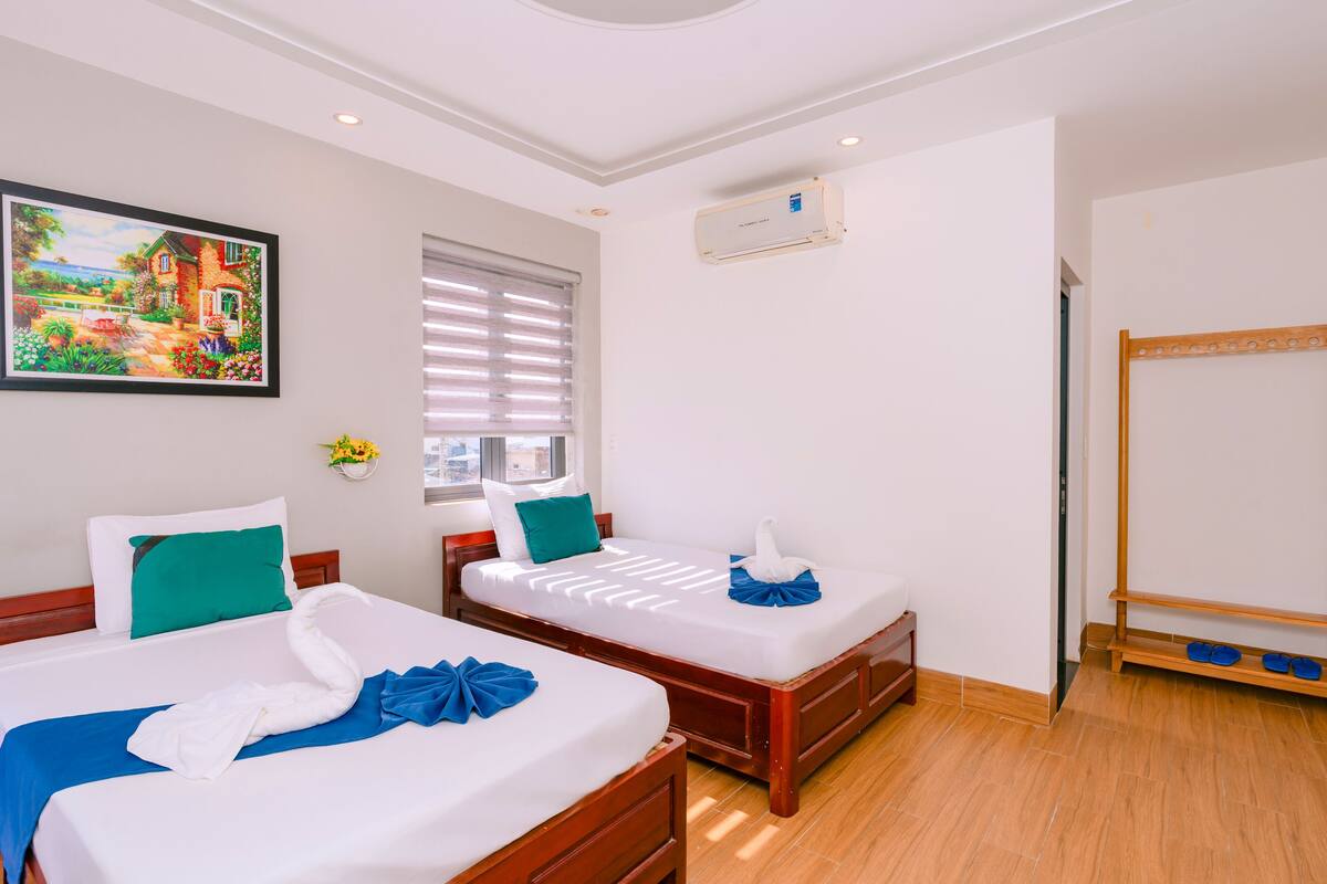 A hotel room with two beds, a wooden floor, a painting on the wall, and a shoe rack.