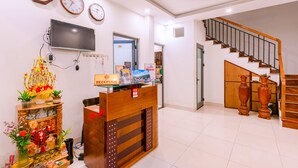 A reception area with a wooden desk, reception sign, wall clocks, a flat-screen TV, and a staircase. - Vinh Khang Homestay (Da Nang)