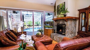Ein Wohnzimmer mit Ledersofas, einem Kamin und Blick auf einen Pool durch große Glasfenster.