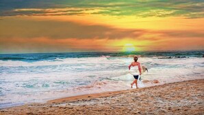 Eine Person rennt am Strand, im Hintergrund Wellen und ein Sonnenuntergang.