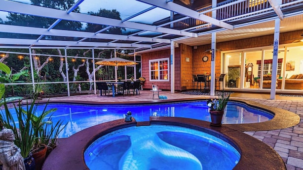 Ein Schwimmbecken mit Whirlpool, umgeben von einer überdachten Terrasse mit Gartenmöbeln und Lichterketten.