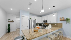 Una cocina moderna con armarios blancos, encimeras de granito y taburetes de bar.