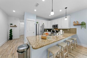 A modern kitchen with white cabinets, granite countertops, and bar stools.