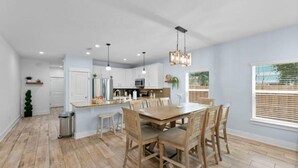 Una cocina moderna con armarios blancos, una mesa de comedor de madera e iluminación colgante.