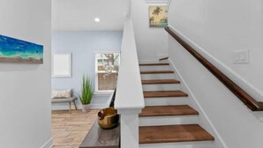 Una escalera moderna con escalones de madera y barandilla blanca, que conduce a una habitación con vistas al exterior.