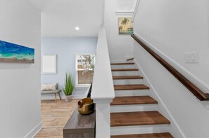 A modern staircase with wooden steps and a white handrail, leading to a room with a view of the outdoors.