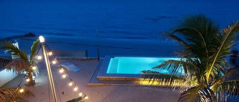 A beachside pool area with a small boat, palm trees, and string lights.