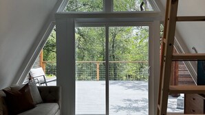 Et værelse med skrå vægge, ventilator i loftet, stor skydedør til en udendørs terrasse og en trætrap.